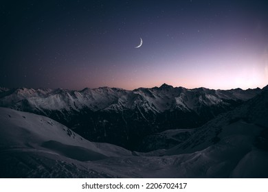 A view of the snowy mountains and the moon at night