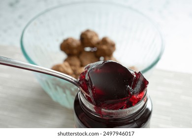 A view of a spoon scooping some grape jelly. A bowl of meatballs are in the background.