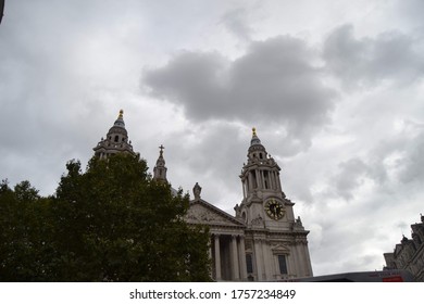 A view of St Paul's Cathedral's Greek revival frontage and bell towers, half obscured by trees. The background is a stormy, cloudy sky. 