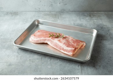 A view of a stack of raw bacon on a baking sheet.