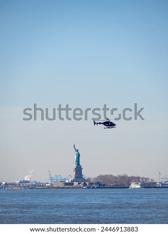 View of the Statue of Liberty from a ferry through Hudson River while a helicopter flies next to the monument. Liberty island skyline with helicopter tour for tourists. New York City sight copy space