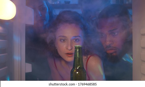 View From Steamy Fridge Of Group Of Friends Opening Refrigerator And Seeing One Beer Bottle Feeling Upset. People Out Of Beer During Party. Young Friends Have No Beer