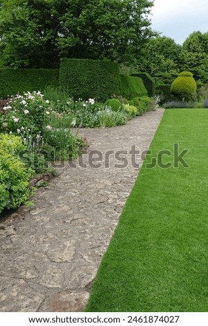 View of a stone paved path in a beautiful garden with a green grass lawn and colourful flowers in bloom
