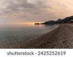 A view of the stone pebble beach and clear water at Letojanni on Sicily at sunsest
