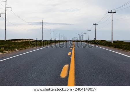 view of a straight yellow dotted line on a paved road in the sand dunes with grass on a cloudy day 
