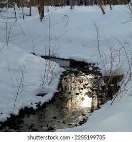 View of a stream in winter with the sun and sky reflecting on the water.