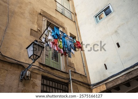 View of a street in Barcelona inside the Gothic quarter. There are clothes hanging from ropes in one of the windows giving color and personality to the street and the neighborhood. Clothes drying