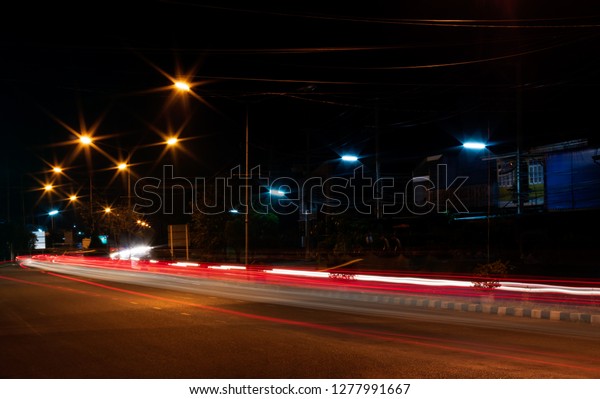 The view of the strip of light from the\
car headlights that pass on the road, which has a lamp installed to\
illuminate the side of the street at\
night.