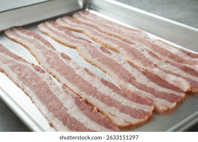 A view of strips of raw bacon on a baking sheet.