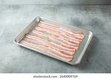 A view of strips of raw bacon on a baking sheet.