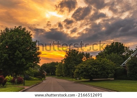 View of suburban Midwestern  neighborhood at sunset in summer; dramatic sky in background
