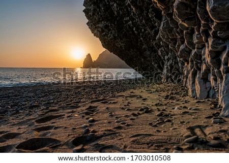 view of the sunset sea and the beach, the rock volcanic rock is lit by the warm sunset, sand and pebbles, volcanic basalt as in Iceland. Jasper beach, cape Fiolent, Crimea