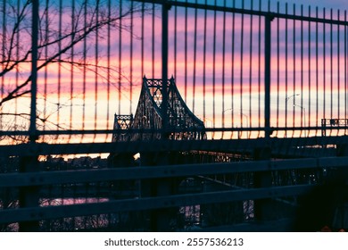 view of a suspended metal bridge on a colourful sunset behind a metal fence - Powered by Shutterstock