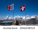 View of the Swiss flag at the top of the Rothorn summit with the beautiful Matterhorn glacier peak at the background. This is the starting point for challenging hikes and a popular spot for sunrise.