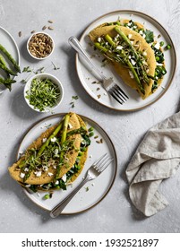 A view of a table with delicious, freshly made vegan crepes ready to be eaten. Made of nutirious chickpea flour, filled with spinach, peas and vegan cheese, topped with grilled asparagus and seeds