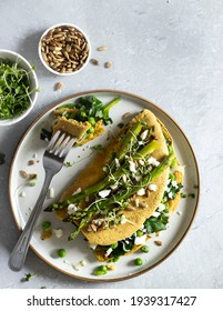 A view of a table with a delicious, freshly made vegan omelette ready to be eaten. Made of chickpea flour, filled with spinach, peas and vegan cheese, topped with grilled asparagus, herbs and seeds