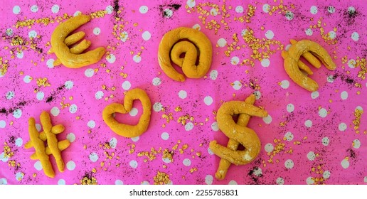 View of a table with different shaped breads: euro, dollar, heart, at, hashtag on a pink tablecloth with white polka dots that symbolizes the relationship between food, the economy and technology
