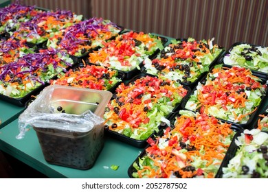 A View Of A Table Featuring Several Trays Of Salad Meal Prep Being Prepared For Catering.