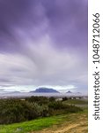 View of  Table Mountain covered in clouds at sunset with a dirt road curving through the landscape, Cape Town, South Africa