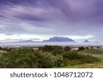 View of  Table Mountain covered in clouds at sunset with a dirt road curving through the landscape, Cape Town, South Africa