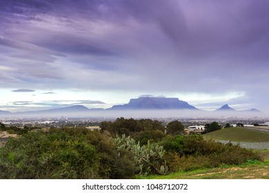 View of  Table Mountain covered in clouds at sunset with a dirt road curving through the landscape, Cape Town, South Africa