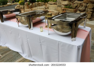 View Of Table Setup For Buffet With White Table Covers, Pink Runner And Empty Chafers. Party Rental Equipment.