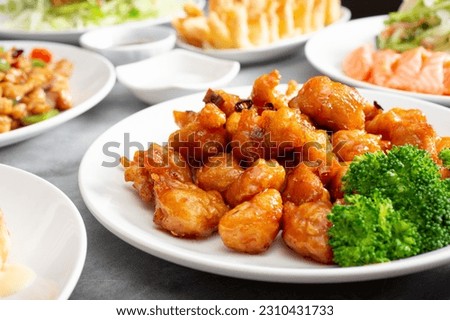 A view of a table of various Chinese entrees, featuring a plate of orange chicken.