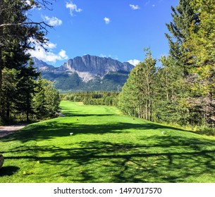 A view from the tee box looking down a tough par 4 lines with trees and the rocky mountains in the background.  It is a beautiful sunny day playing golf in Kananaskis.