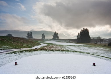 View from the tee of a golf course in Scotland on a snowy winter morning, with dramatic cloudy sky overhead.