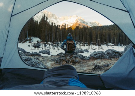 View from the tent on tourist and sporty outdoor clothes in blue jacket. Mountain view from morning in snowy landscape. Tourist mood