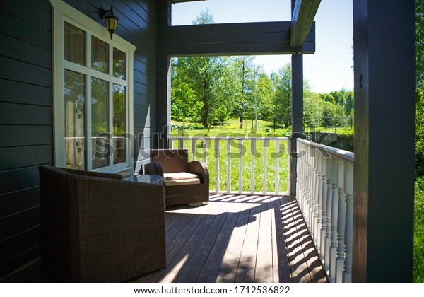 View from the\
terrace of a country wooden house to the garden through the white\
wooden railing of the terrace. Verandah of a house in a Park in\
summer among trees and\
bushes