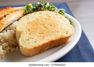 A View Of A Thick Slice Of Garlic Toast, Part Of A Seafood Entree, In A Restaurant Or Kitchen Setting.