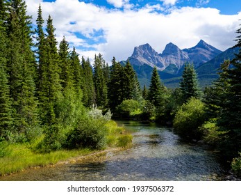 View Of Three Mountain Peaks In The Distance With A River In The Foreground