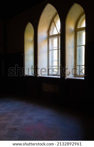View of three neo-gothic windows with beautiful wooden frames in the interior of a dark room in Sharovsky castle, Ukraine.