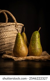 View of three pears on a table with a basket, black background, vertical, with copy space