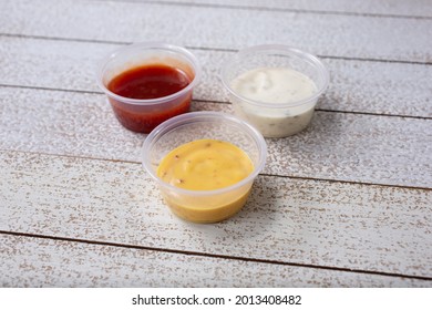 A View Of Three Sauces In Plastic Condiment Cups, Featuring Ranch Dressing, Honey Mustard, And BBQ Sauce.