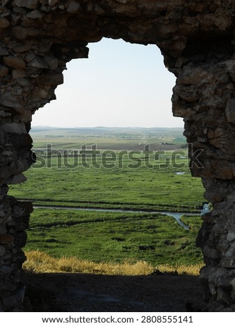 View through an ancient stone window overlooking green wetlands and countryside landscape