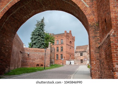 View through the arched entry of the Bridge Gate (Brama Mostowa) to Torun old town, Poland. Ancient, medieval gate, erected in 1432, part of the city wall. Red brick, gothic buildings, cityscape