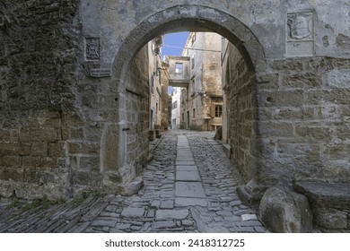 View through an arched gateway along a cobbled street into an ancient village without people during the day - Powered by Shutterstock