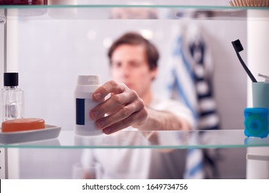 View Through Bathroom Cabinet Of Man Taking Medication From Container
