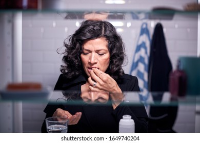 View Through Bathroom Cabinet Of Mature Woman Taking Medication With Glass Of Water