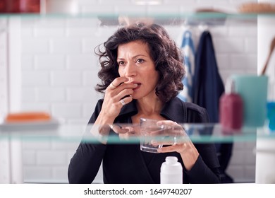 View Through Bathroom Cabinet Of Mature Woman Taking Medication With Glass Of Water