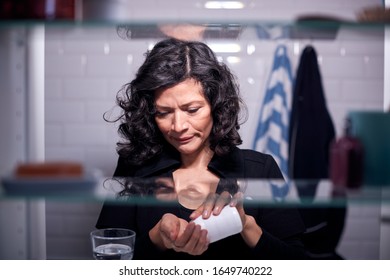 View Through Bathroom Cabinet Of Mature Woman Taking Medication From Container