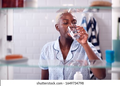 View Through Bathroom Cabinet Of Woman Drinking Glass Of Water