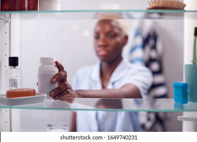 View Through Bathroom Cabinet Of Young Woman Taking Medication From Container