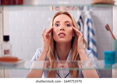 View Through Bathroom Cabinet Of Young Woman Getting Ready For Work Applying Moisturiser