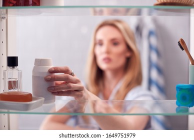 View Through Bathroom Cabinet Of Young Woman Taking Medication From Container