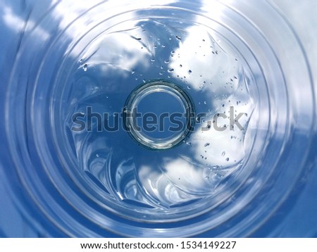 View of through the bottom of the PET water bottle with white clouds and blue sky as the background.
Point of view selected to focus object and abstract background.