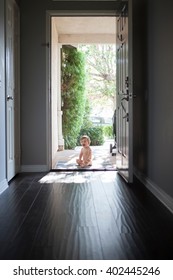 View Through Entrance Hall Of Baby Boy Sitting Outside At Open Front Door, Looking At Camera Open Mouthed