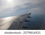 View through the flying plane window on a beautiful blue skyscape, shining sun, and airplane wing. Travel time and transport concept.